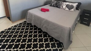 Een slaapkamer met een bed, nachtkastje, een tapijt met dessin en een deur.