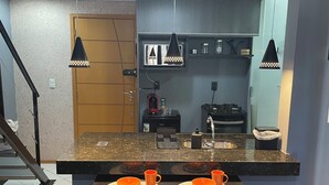 Een compacte keuken met een aanrecht, twee zwarte stoelen en een kleine eettafel.