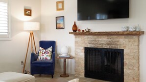 A living room with a blue armchair, a white sofa, a fireplace, and a mounted TV.