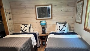 A room with two beds, wooden walls, a small table with a lamp, and a framed picture on the wall. - Fisherman’s paradise waterfront. Boat ramp on property sleeps 6.      2-2.  (Many)