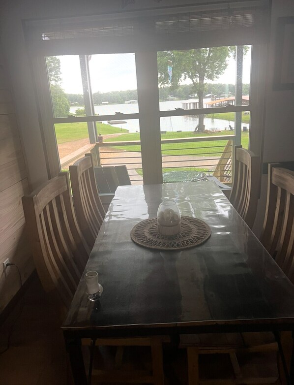 A dining table with chairs, a glass, and a pitcher, set against a view of a lake and grassy area.