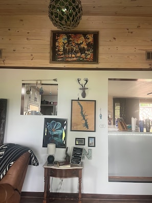 Une pièce avec un plafond en bois, un tableau représentant un cerf encadré, une carte du réservoir de Toledo Bend, un panneau d’accueil et une table avec une lampe et un livre.