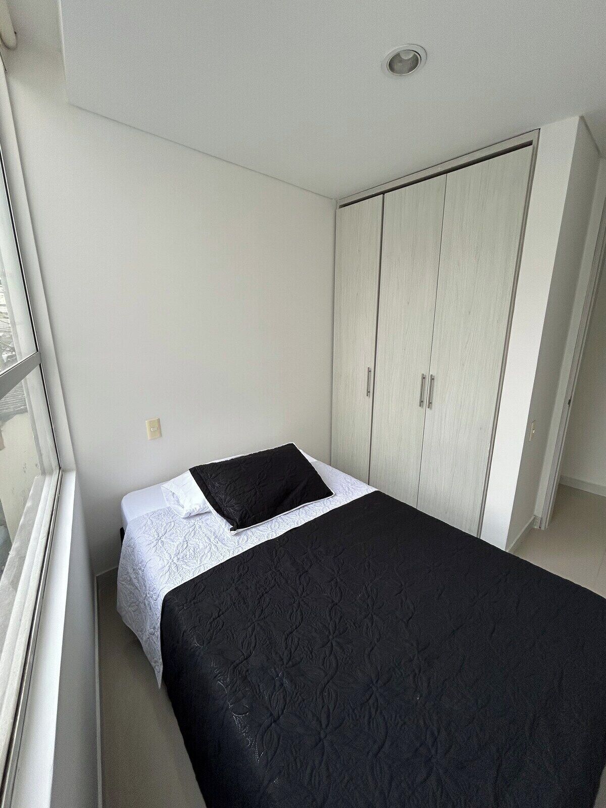 Una habitación pequeña con cama individual, pared blanca, ventana y armario.