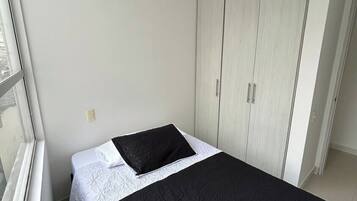 Una habitación pequeña con cama individual, pared blanca, ventana y armario.