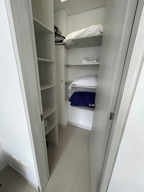 Un vestidor estrecho con varias repisas y una cama.