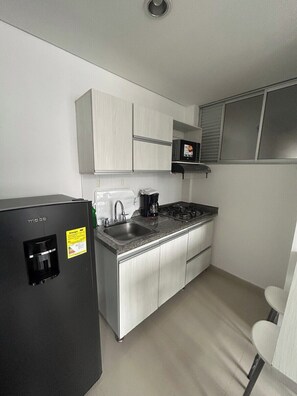 Cocina compacta con refrigerador, microondas, lavamanos y estufa.