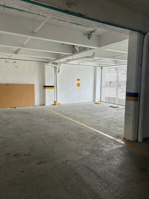 Un estacionamiento vacío con pisos de concreto, paredes blancas y algunas marcas amarillas y negras.