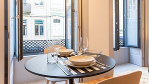 A dining table set with plates, glasses, and cutlery, positioned near large windows with a view of buildings. - Modern Retro Downtown by LovelyStay (Porto)