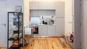 A compact kitchen with a built-in oven, a coffee machine, and a sink. There is a metal shelf unit with dishes and glasses, and a fire extinguisher mounted on the wall. - Modern Retro Downtown by LovelyStay (Porto)