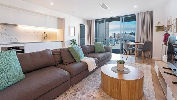 A modern living room with a brown sofa, a round wooden coffee table, and a city view through large windows.
