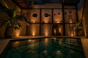 A pool area with a geometric pool design, potted plants, and a building with circular windows and a lattice design. - Capybara Hostel (Villavicencio)