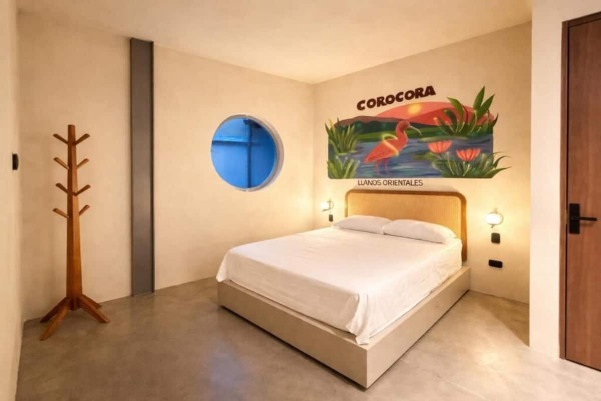 A bedroom with a bed, a wooden coat rack, a circular window, and a wall mural.