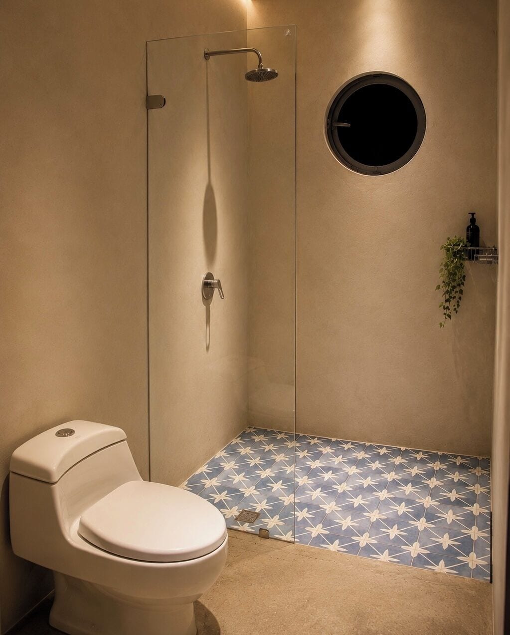 Un bagno con un water, una doccia con porta in vetro e uno specchio tondo.