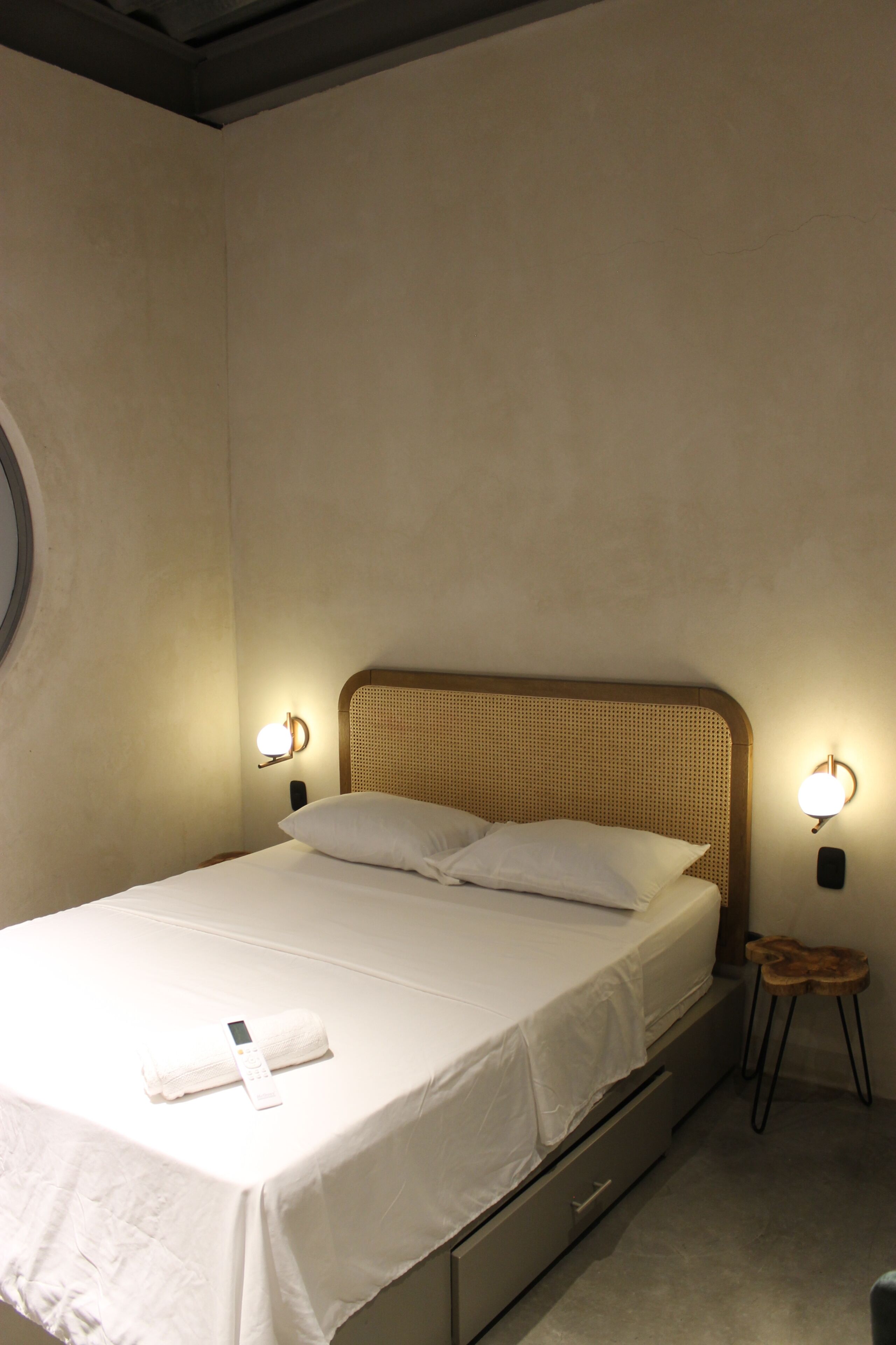 A single bed with a headboard, two bedside lamps, a small stool, and a bedside table with a remote control.