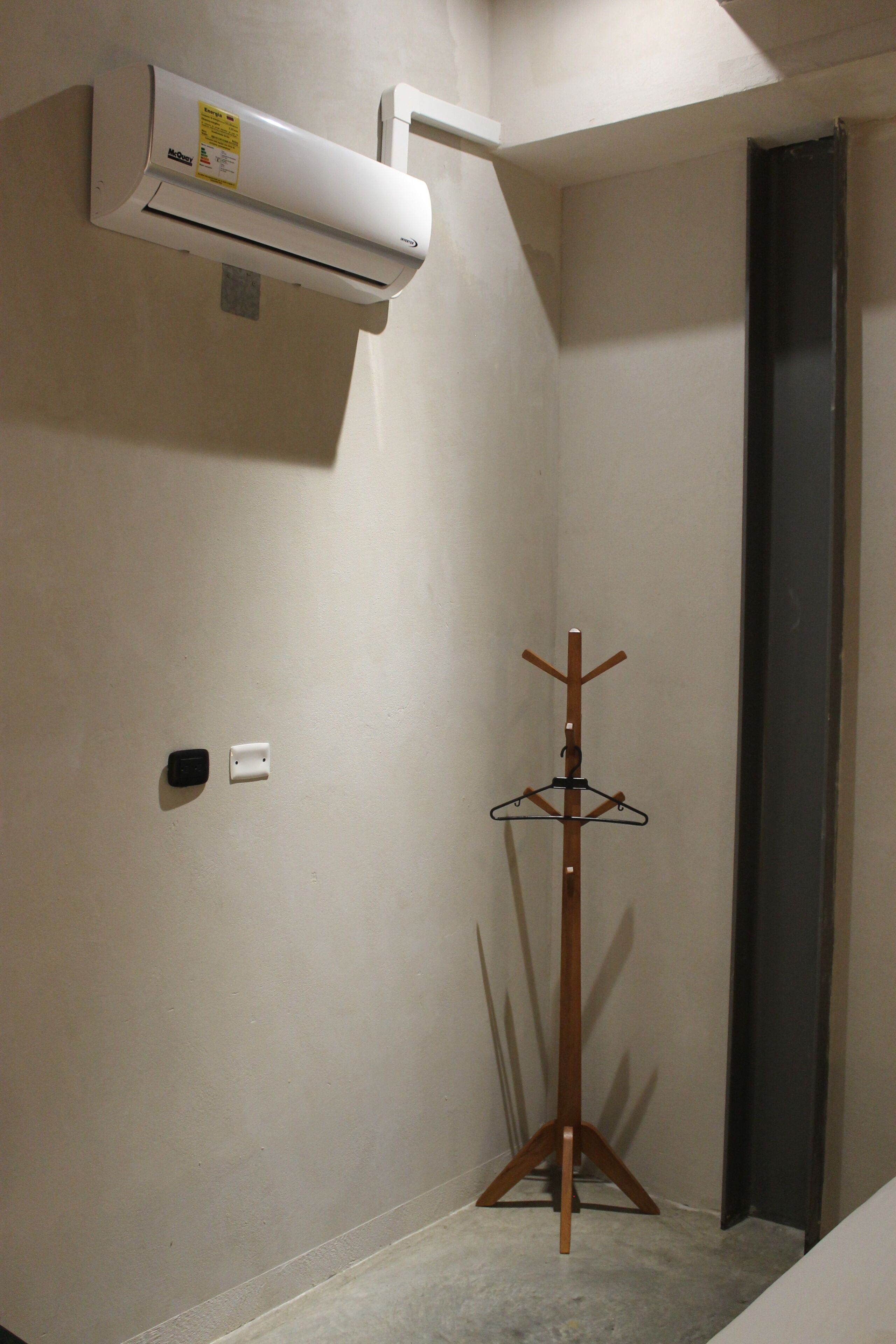 Un coin de pièce avec un mur blanc, un porte-manteau en bois, un appareil de climatisation blanc et un cadre de porte.