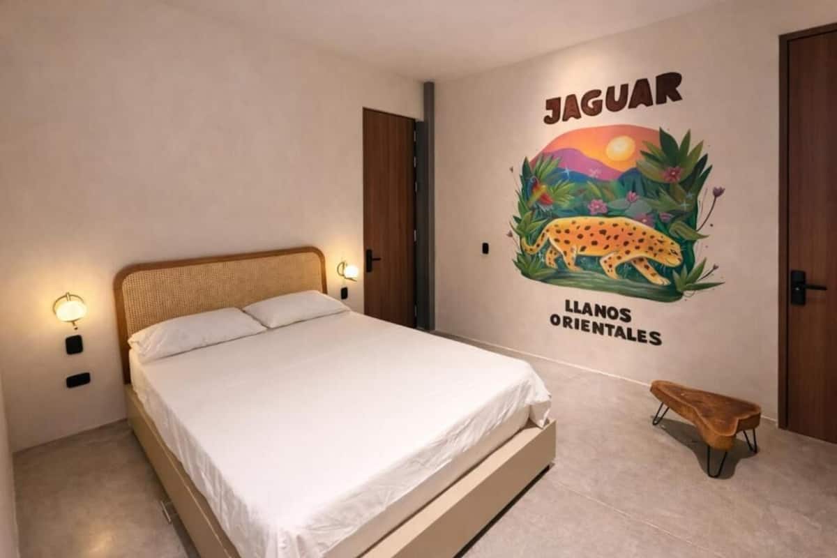 A bedroom with a bed, a wall mural of a jaguar, and a small bench.