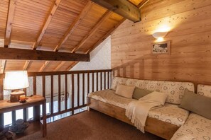 Interior acolhedor de uma cabana de madeira, com teto de madeira, um banco estofado, um abajur e uma moldura na parede.