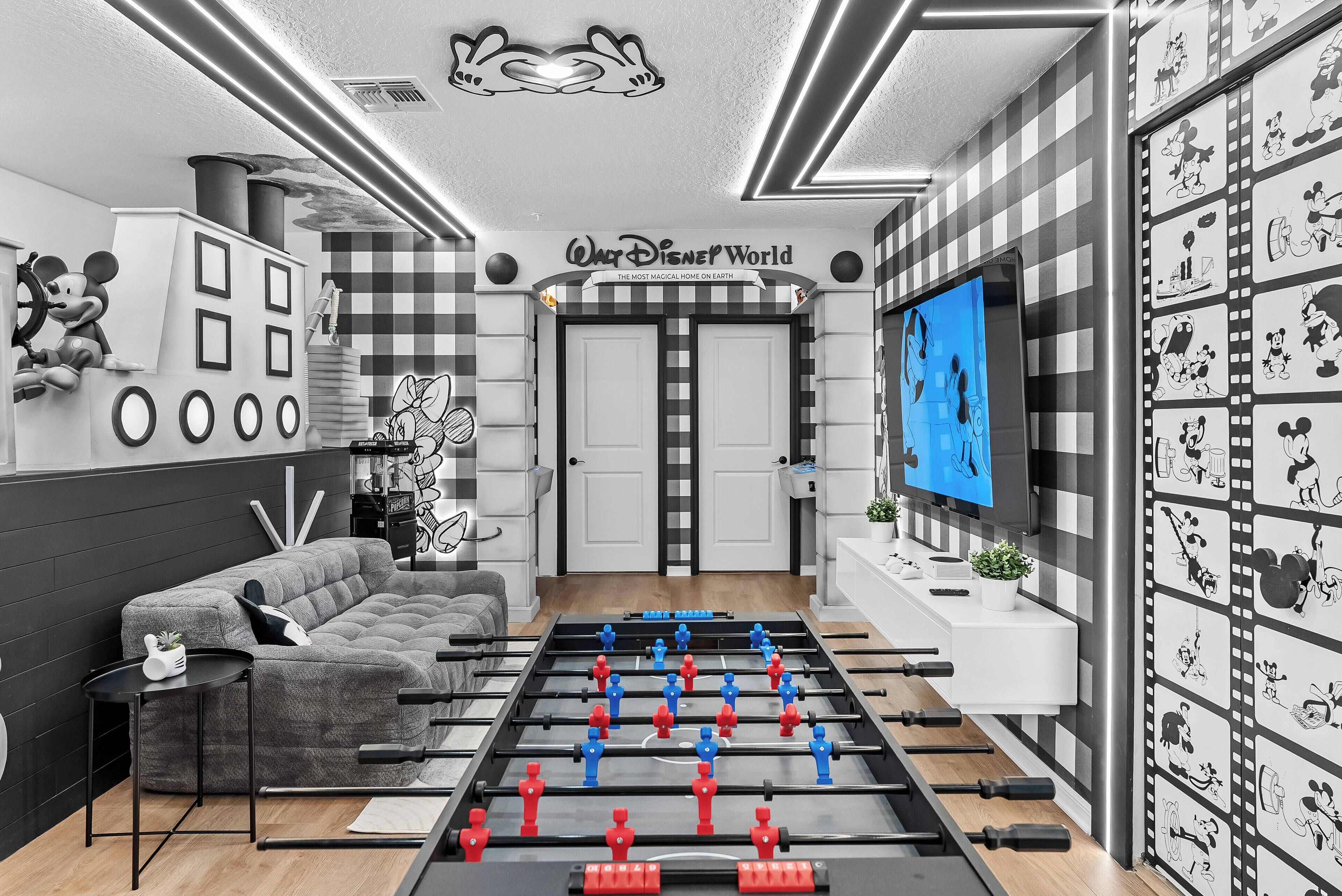 A room with a foosball table, a television, and a wall with Disney characters.