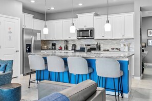 Cozinha moderna com armários brancos, geladeira de aço inoxidável, micro-ondas e uma ilha azul com banquetas.