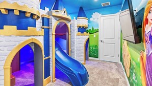 A children's play area with a blue slide, castle-themed play structures, and a door with a mural. - 10BR house at Windsor Cay resort, clermont (Clermont)