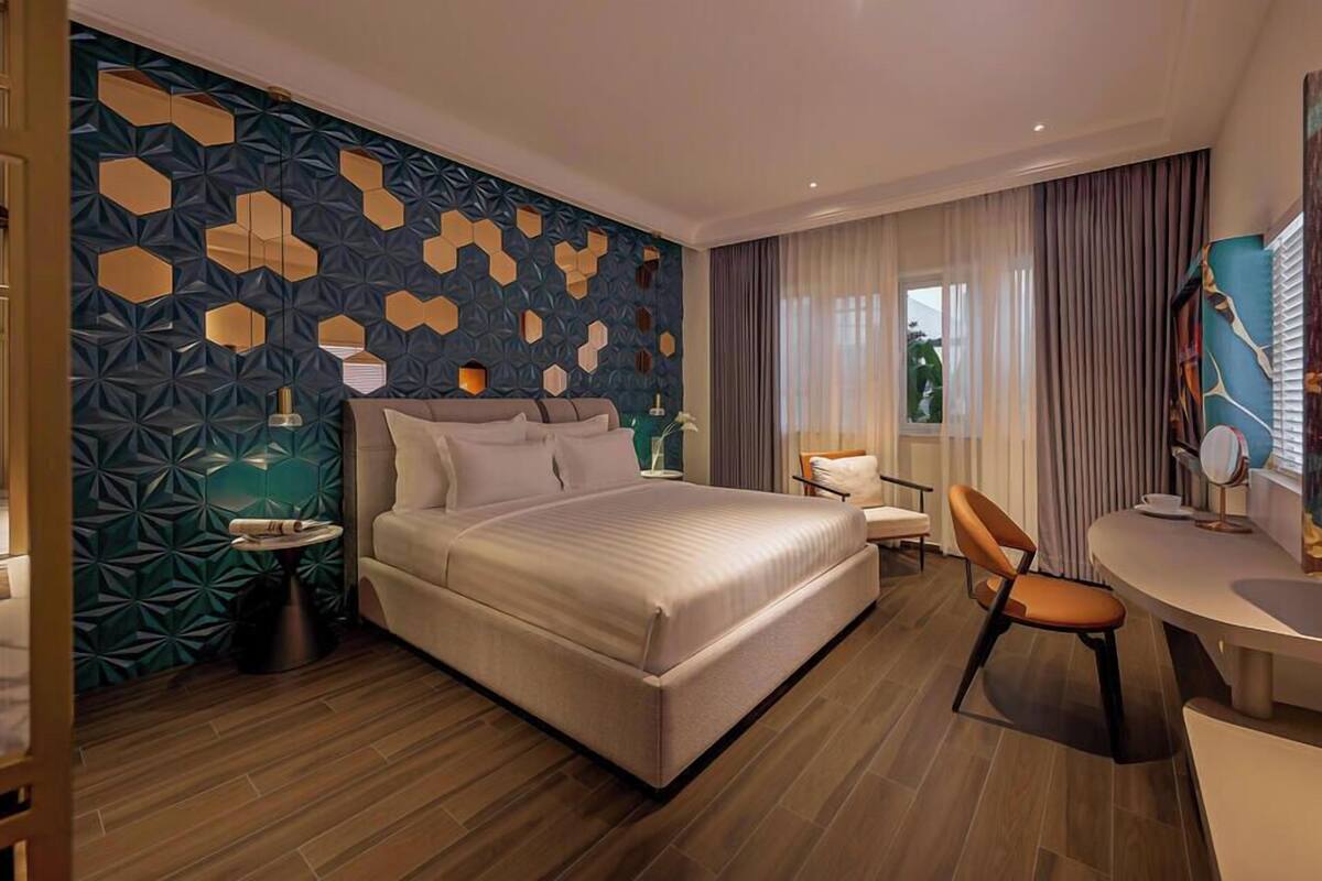 Quarto de hotel moderno com uma cama grande, uma escrivaninha, uma cadeira e um detalhe decorativo na parede.