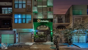 Un hôtel à la façade moderne, doté de nombreux balcons et d’une entrée imposante surmontée d’une arche verdoyante.