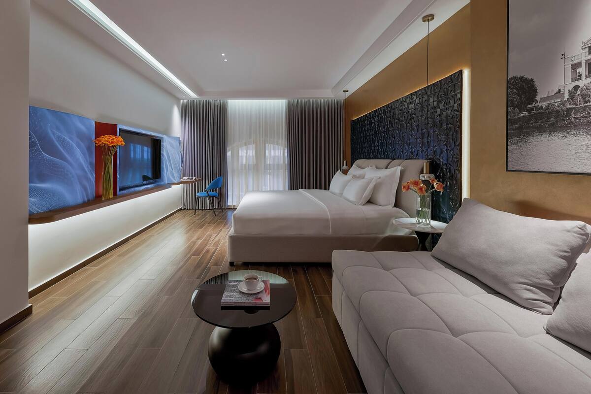 Quarto de hotel moderno com uma cama grande, um sofá, uma mesa de centro e uma televisão.