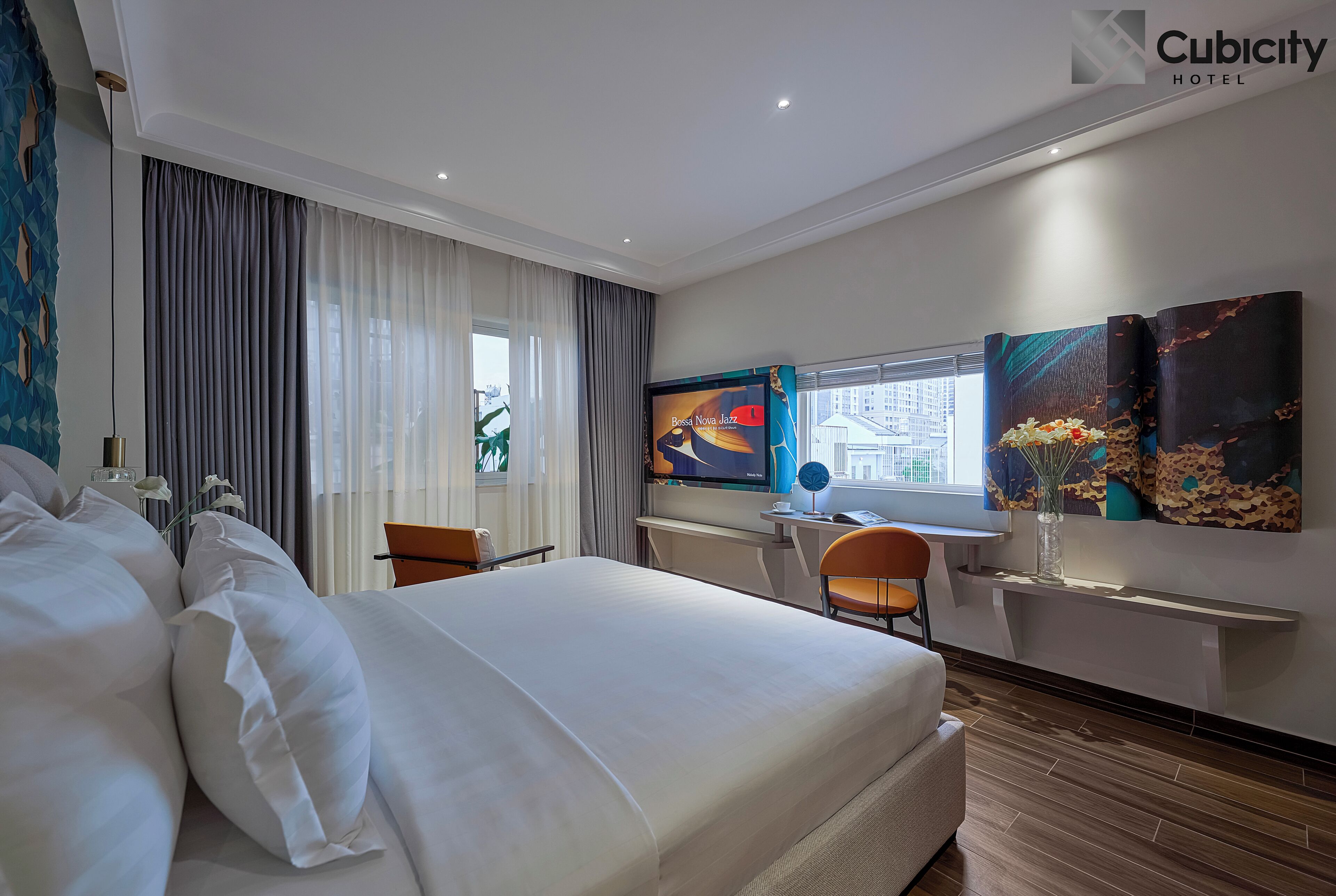 Une chambre d’hôtel avec un grand lit, un bureau avec une chaise, une télévision et des œuvres d’art accrochées aux murs.