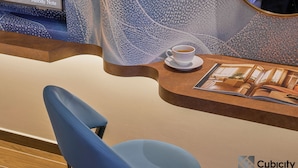 Un área de recepción de hotel moderna con una silla azul, una taza de café sobre un platillo y una revista en la mesa.