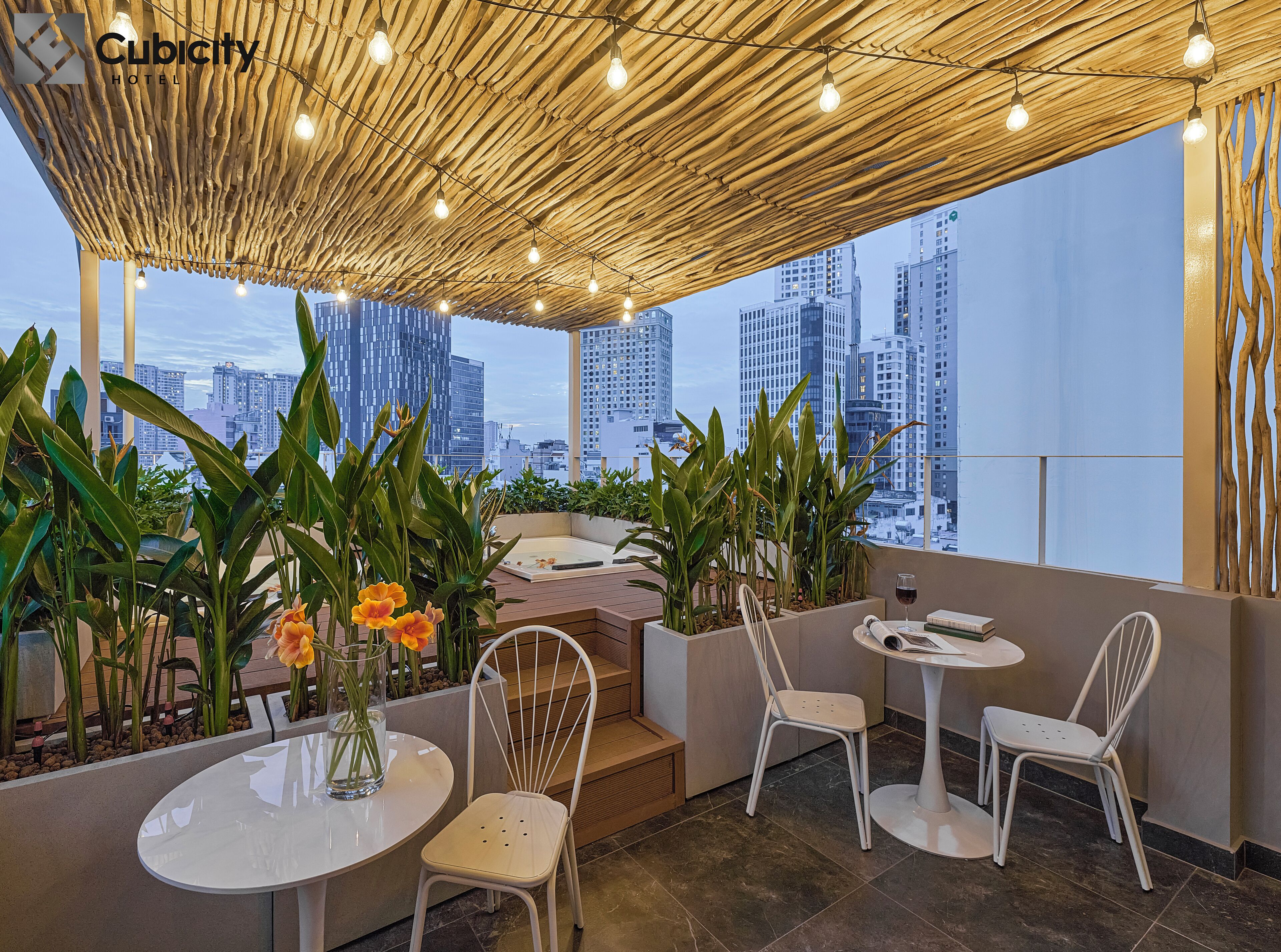 Une terrasse sur le toit offrant une vue sur les bâtiments de la ville, avec un plafond en bois, des plantes en pot et des chaises blanches.
