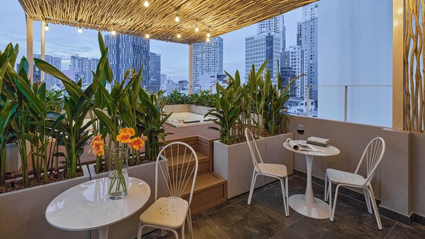 A rooftop terrace with a view of city buildings, featuring a wooden ceiling, potted plants, and white chairs.