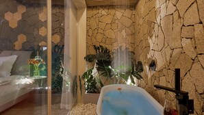 A modern bathroom with a red bathtub, white pebbles, and a glass shower enclosure.