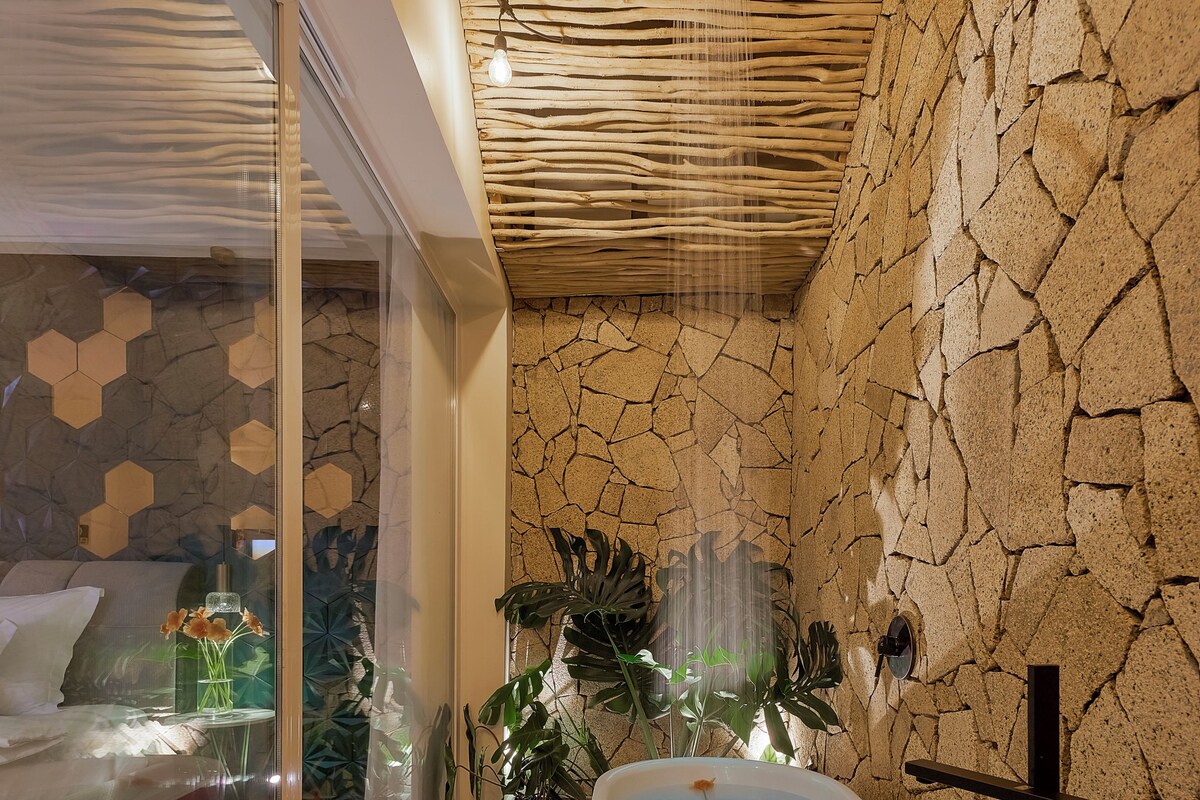 A modern bathroom with a red bathtub, white pebbles, and a glass shower enclosure.