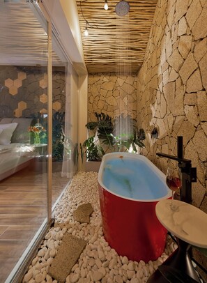 A modern bathroom with a red bathtub, white pebbles, and a glass shower enclosure.