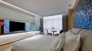 Una habitación de hotel moderna con una cama grande, un televisor de pantalla plana, una pequeña mesa con sillas y un panel decorativo en la pared.