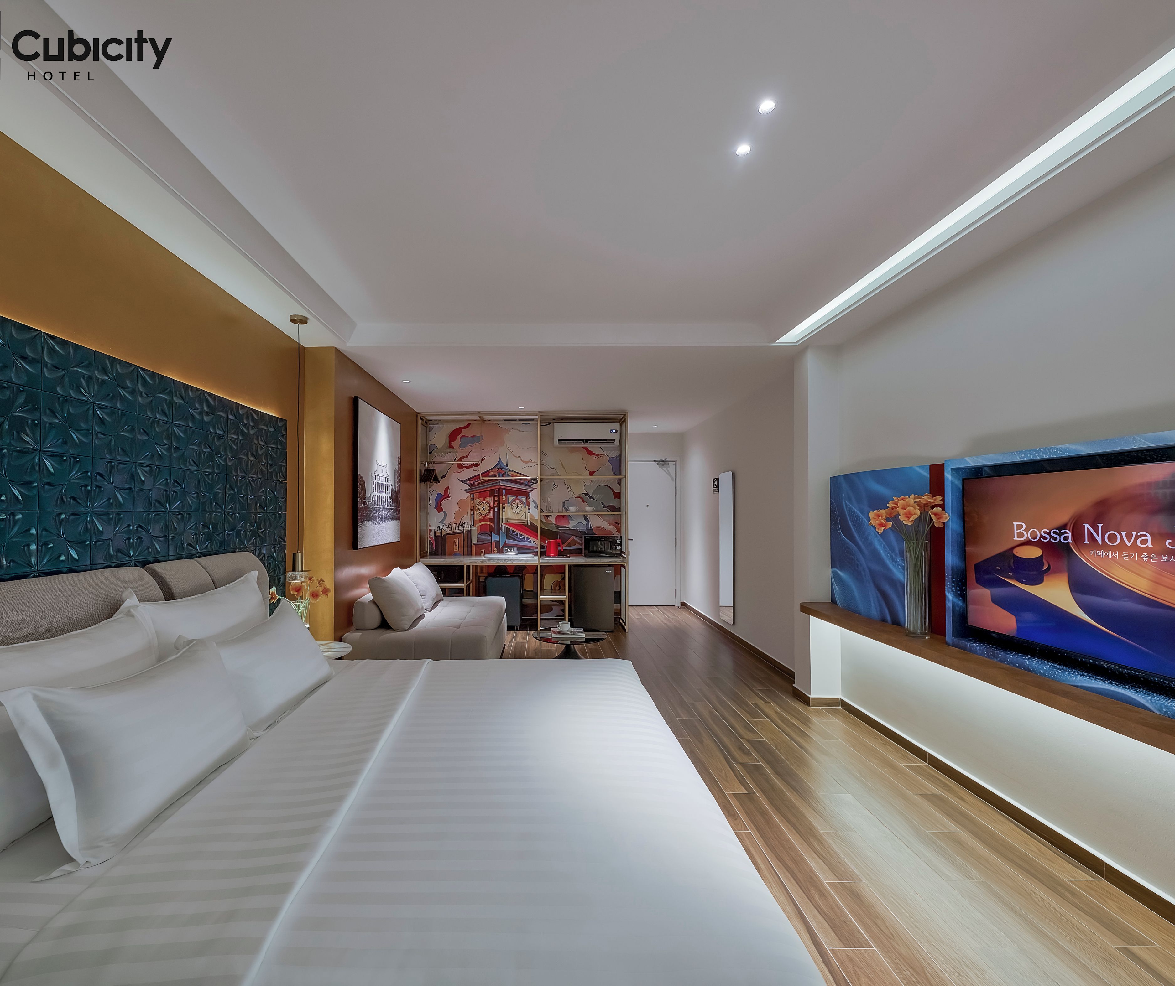 A modern hotel room with a large bed, a sofa, a TV, and a decorative wall.