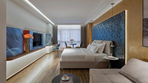 Une chambre d’hôtel moderne avec un grand lit, un canapé, une petite table avec une tasse et un téléviseur fixé au mur.