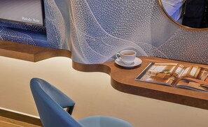 A modern hotel reception area with a blue chair, a coffee cup on a saucer, and a magazine on the table.