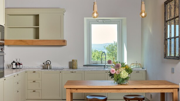 A kitchen with a wooden table, a window with a view, and pendant lights.