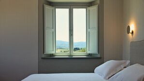 A bedroom with a large window, a bed, and a wall-mounted light.