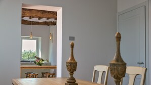 A wooden dining table with two chairs, a window with a view of greenery, and a wooden ceiling beam.