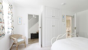 A bedroom with a bed, a wicker chair, a dresser, and a white wardrobe. - Sail Loft (Marine Parade - St Mawes) (St Mawes)