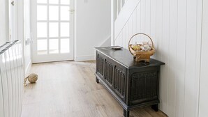 A hallway with a wooden floor, a dark wooden cabinet, a white door, and a white wall with a clock. - Sail Loft (Marine Parade - St Mawes) (St Mawes)