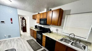 A compact kitchen with wooden cabinets, a microwave, a stove, and a sink. - Delightful 5-bedroom house Tampa (Tampa)