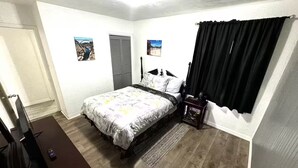 A bedroom with a bed, a nightstand, a window with black curtains, and two wall-mounted pictures. - Delightful 5-bedroom house Tampa (Tampa)