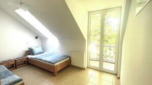 Un dormitorio pequeño y luminoso con techo inclinado, una cama individual, una mesita de noche y vistas a un espacio exterior a través de una puerta corrediza de cristal.