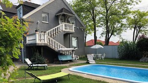 Una casa con piscina, un área de estar techada al aire libre y una escalera que lleva a un balcón.