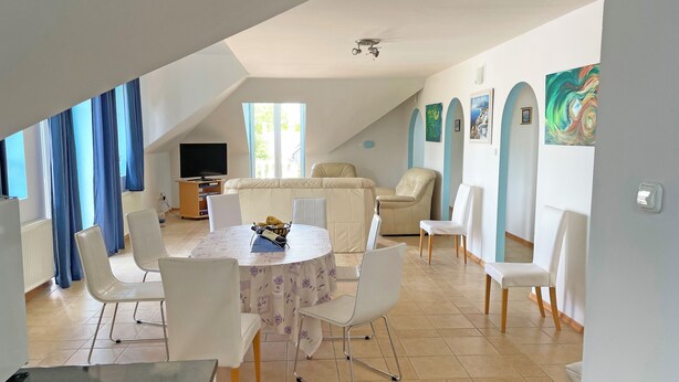Un salón amplio con techo alto, una mesa de comedor rodeada de sillas, un sofá y un televisor.