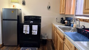 Una cocina con refrigerador, estufa, lavaplatos, gabinetes de madera y una alfombra estampada.