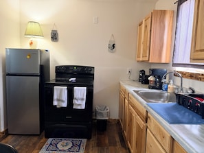 A kitchen with a refrigerator, stove, sink, wooden cabinets, and a patterned rug.